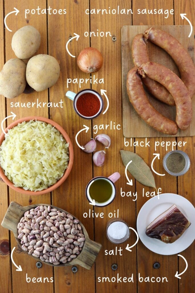 Gathering ingredients for Slovenian jota soup: sauerkraut, potatoes, dried beans, smoked bacon, carniolan sausages, garlic, onion, paprika, black pepper, salt and bay leaves.